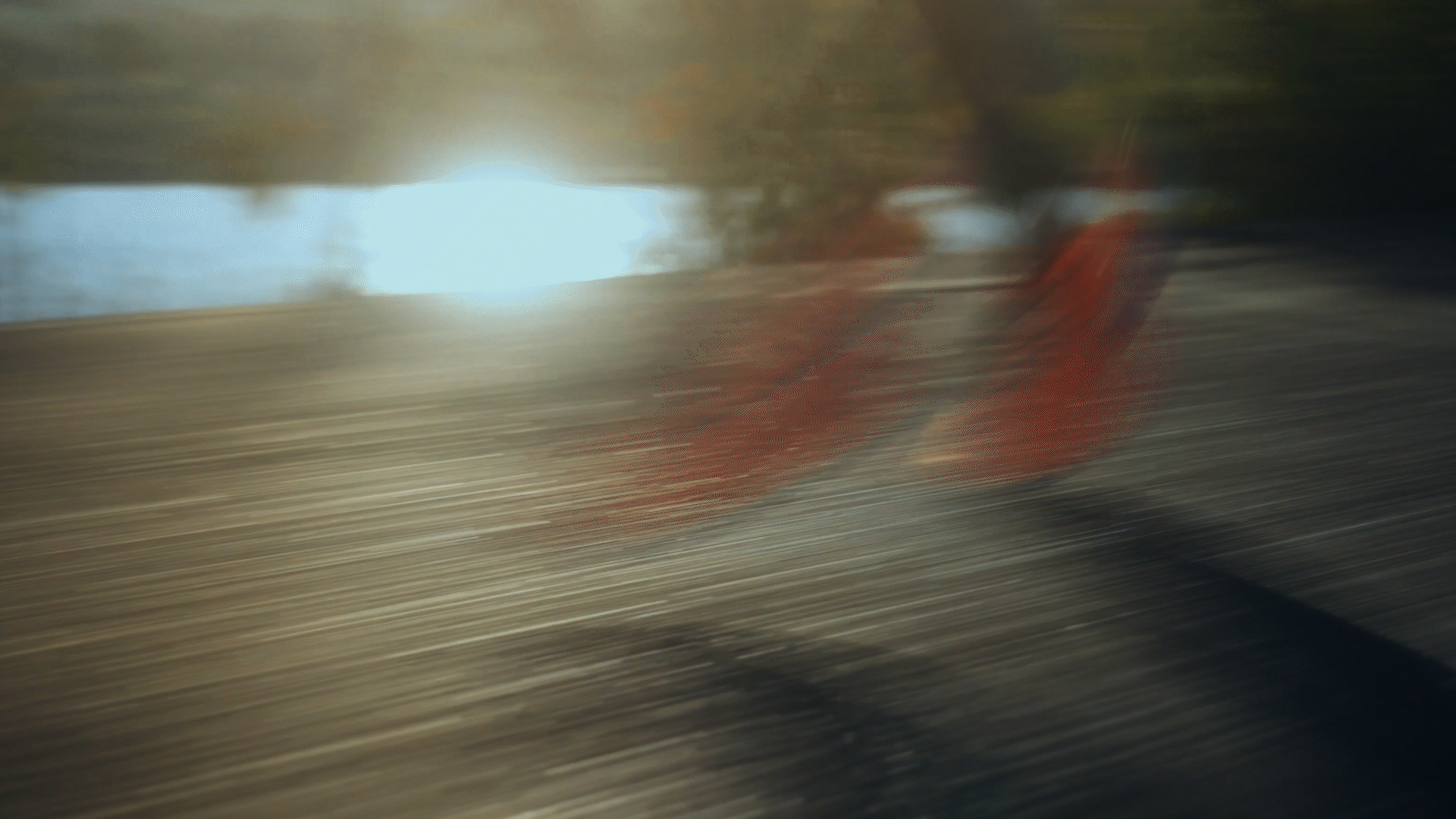 A blurry image of a snowmobile with a red stripe moving quickly on snow, with trees and sunlight in the background.