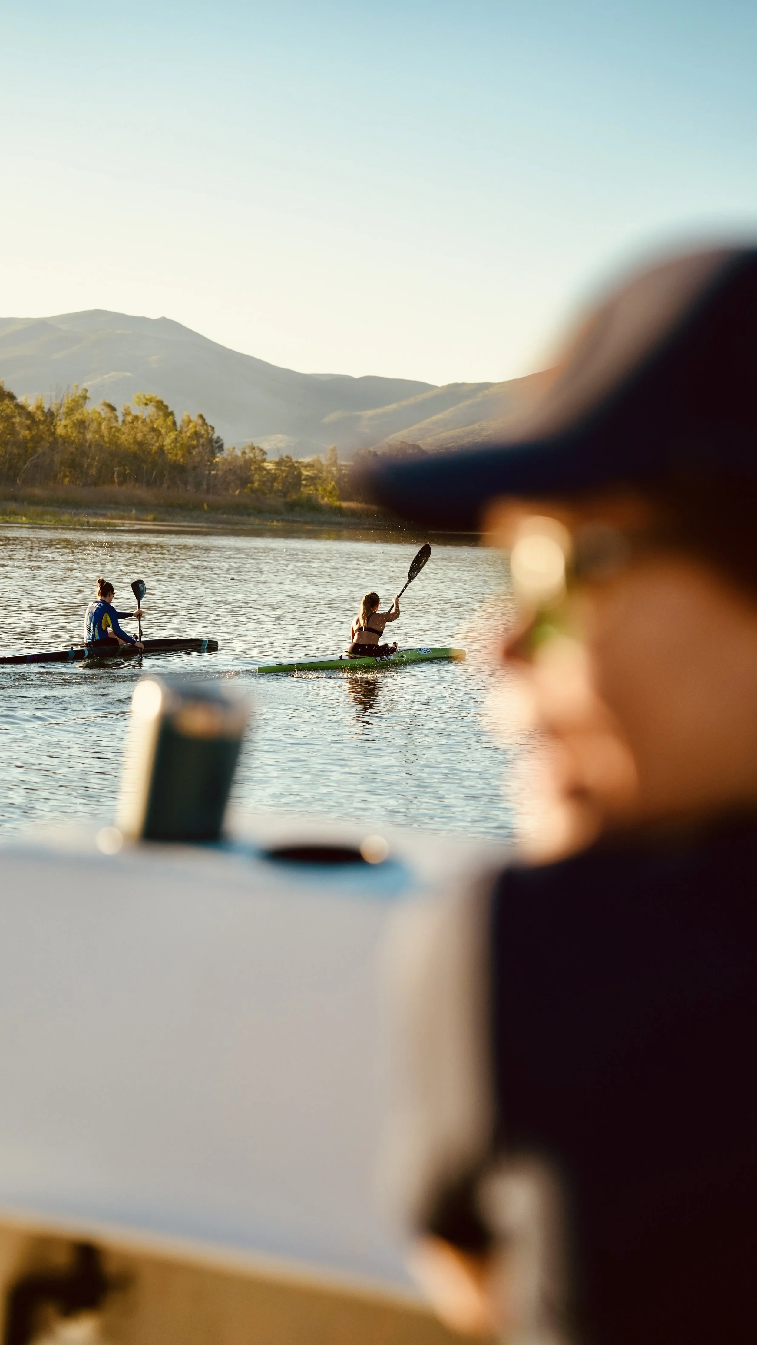 People kayaking on a river with mountains in the background, viewed from the perspective of someone on a boat or dock.