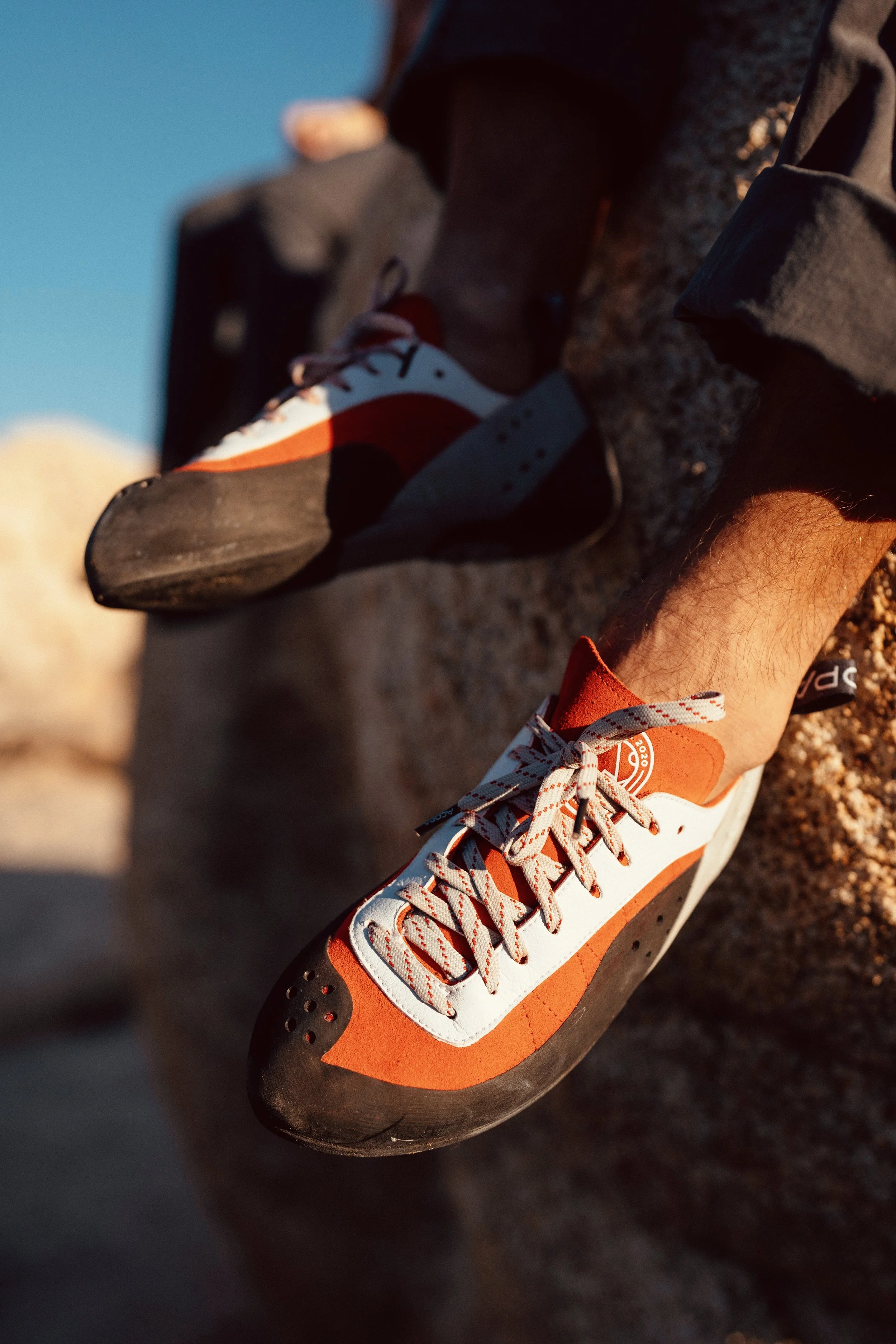 Close-up of a pair of athletic shoes, orange and white, on a rocky surface, with one shoe prominently displayed in the foreground.