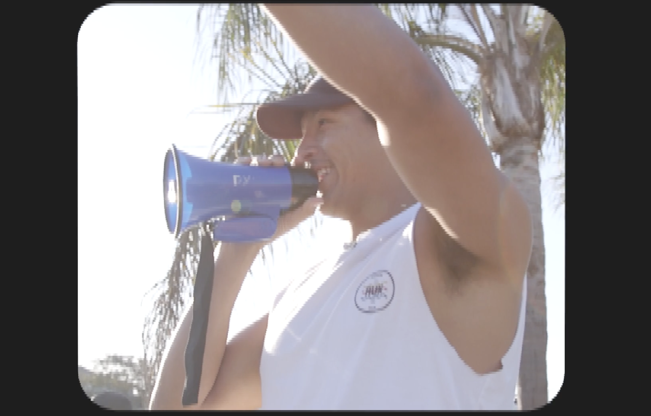 A man wearing a white sleeveless shirt and a blue cap, sweating, outdoors near water and palm trees.