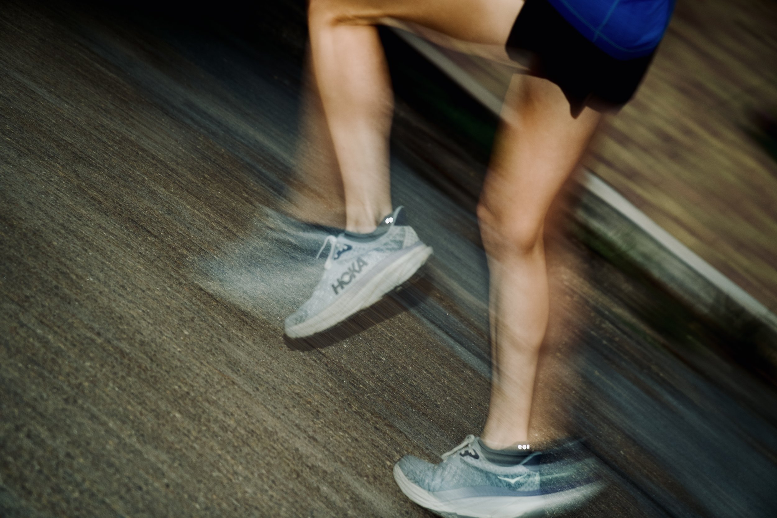 Reflection of a person wearing gray sneakers with black accents and white soles, standing on a dark brown wooden floor.