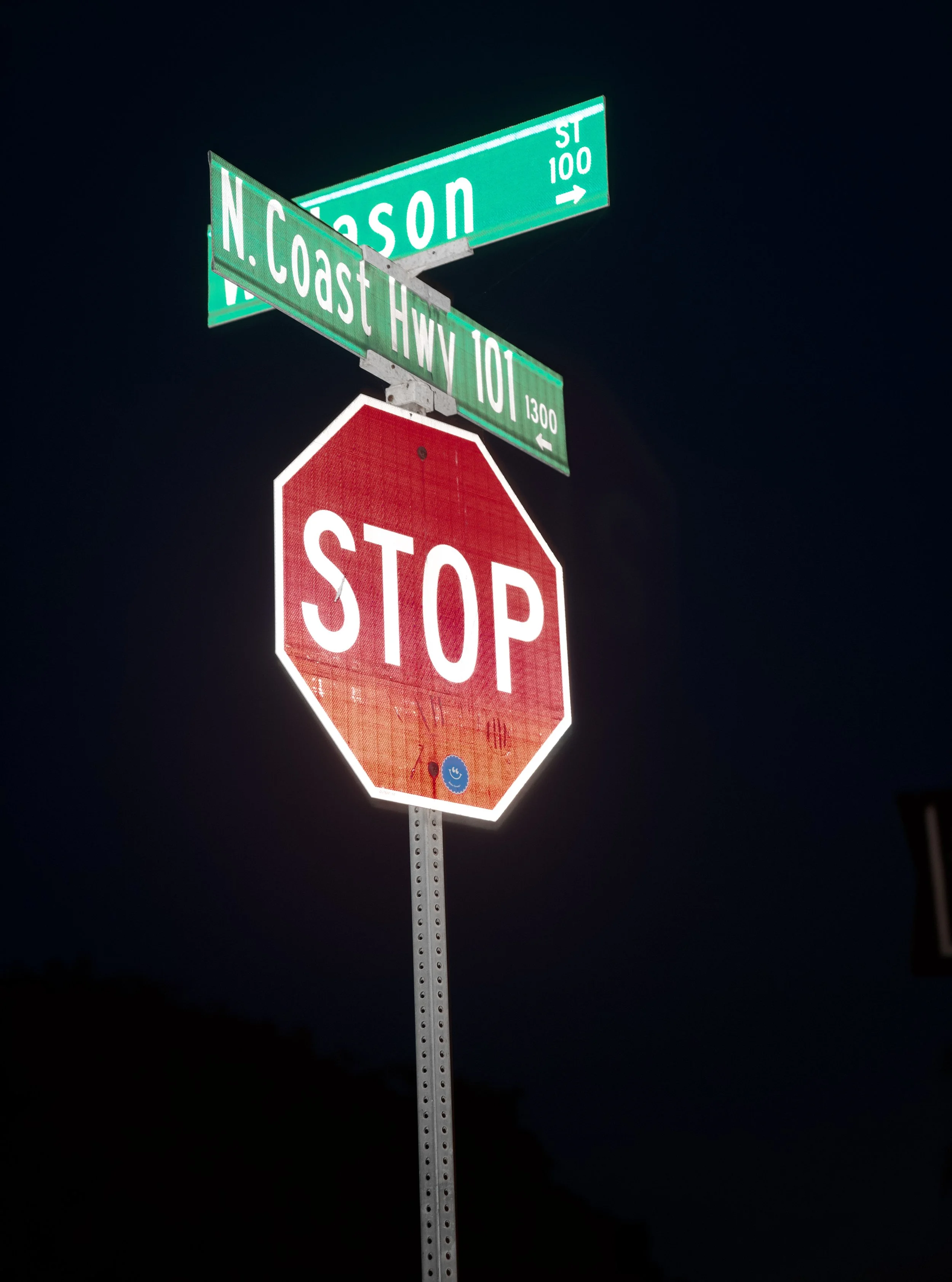 Street signs at night indicating the intersection of North Coason and 10th Street, with a red stop sign below.