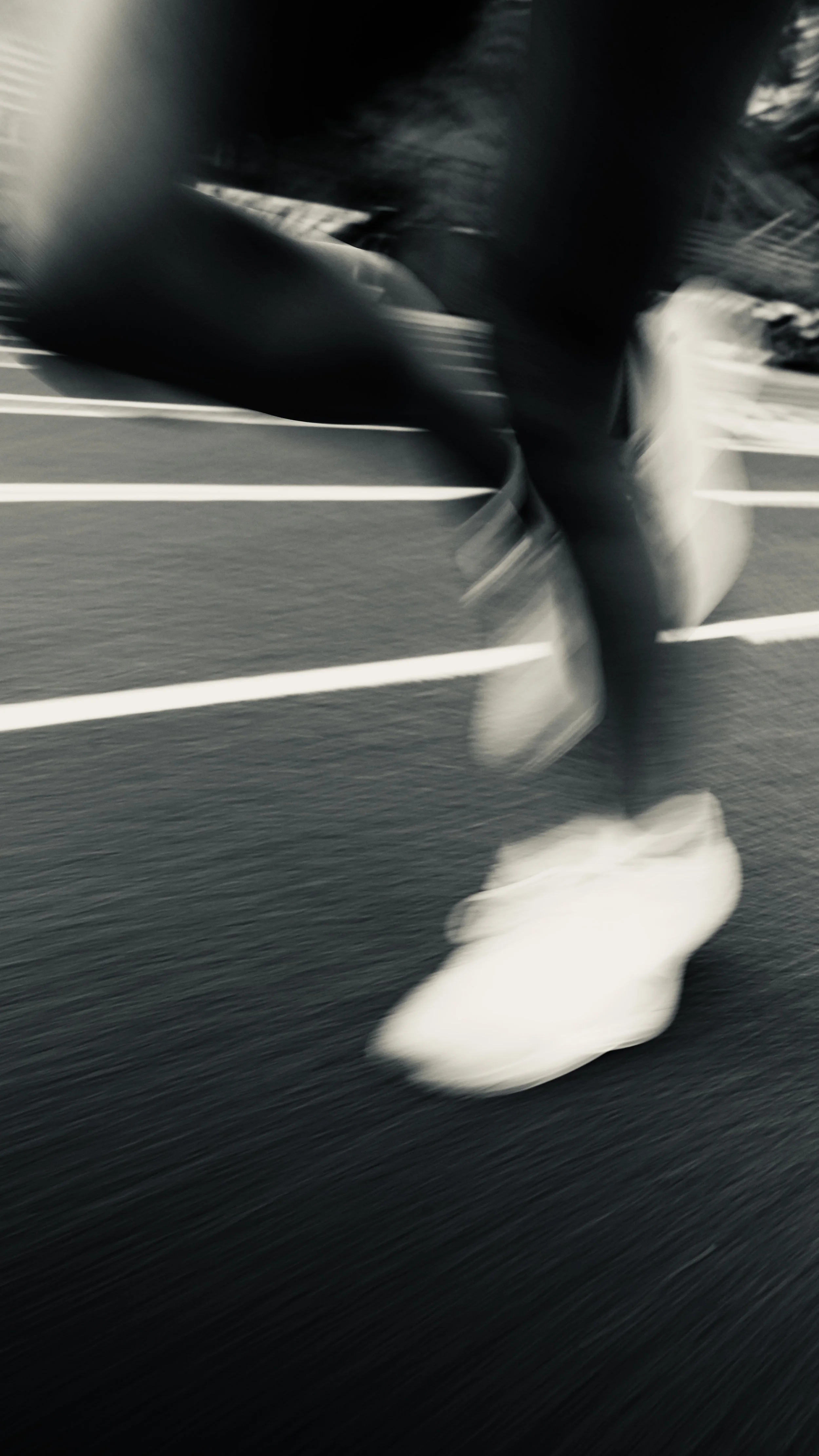 Blurred motion of a person walking on a paved surface with white parking lot lines, wearing light-colored clothing.