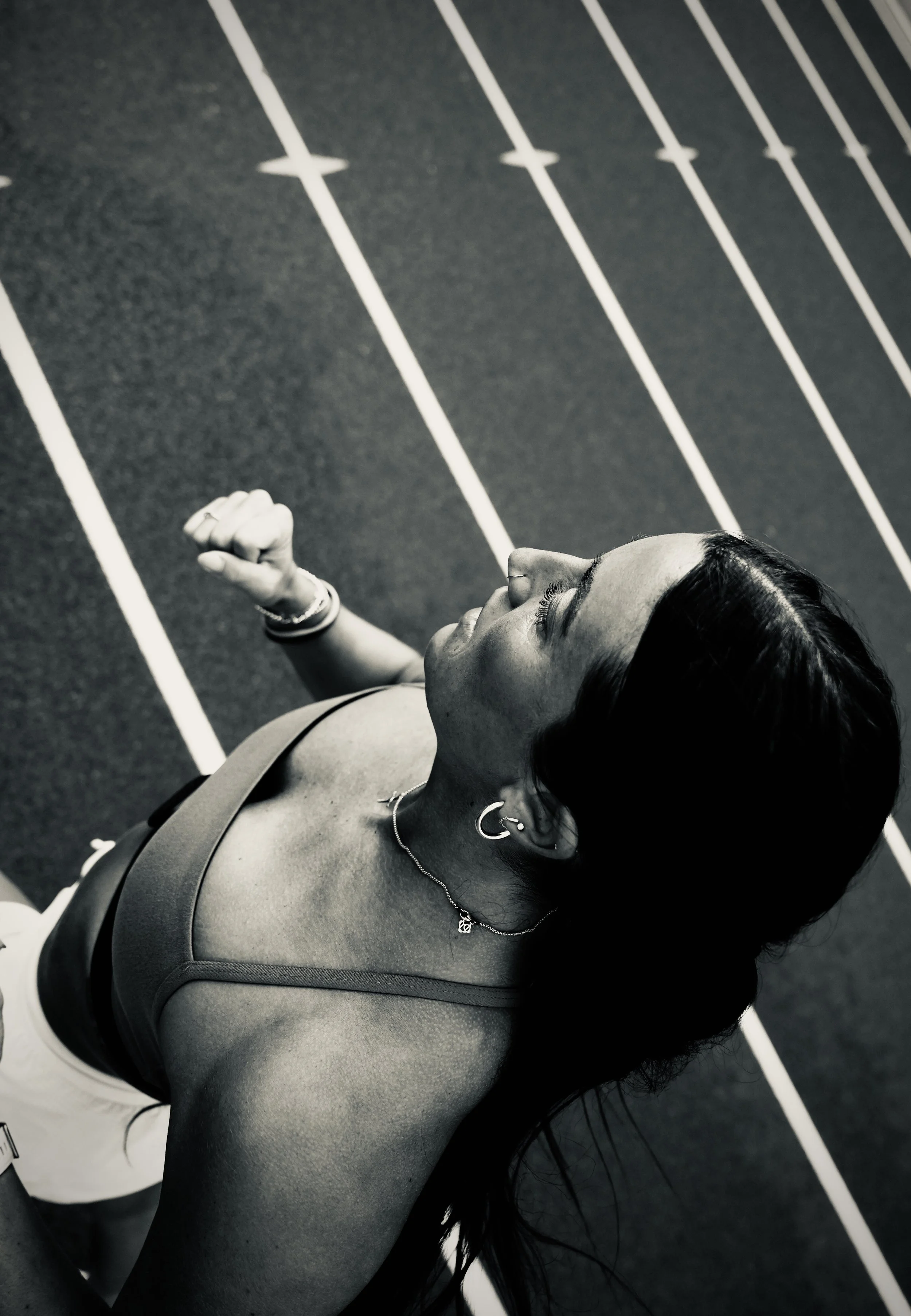 A woman at a track field, looking upward, with her left arm raised and clenched fist.