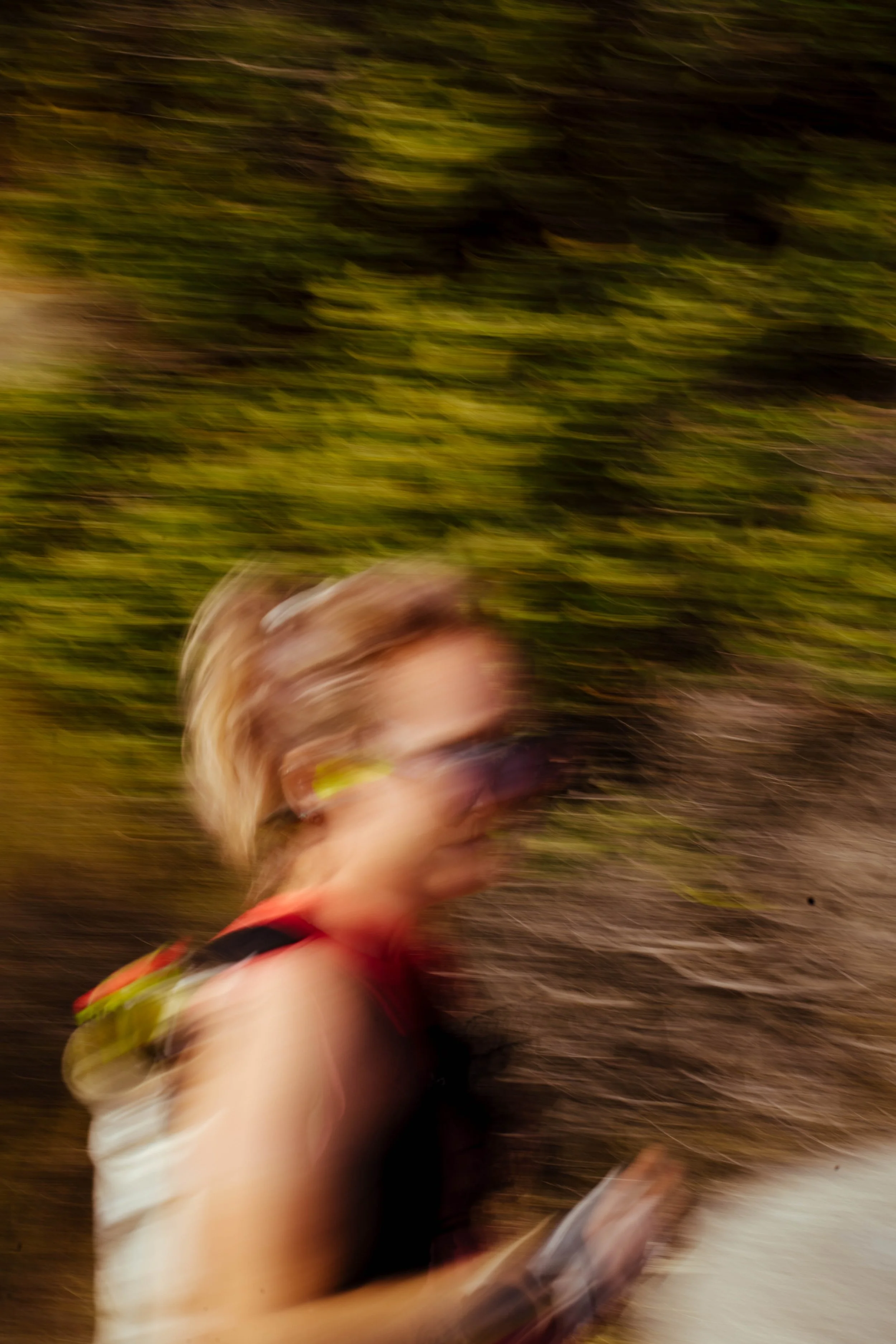 A person running outdoors with motion blur causing the image to look blurry and streaked, with green trees in the background.