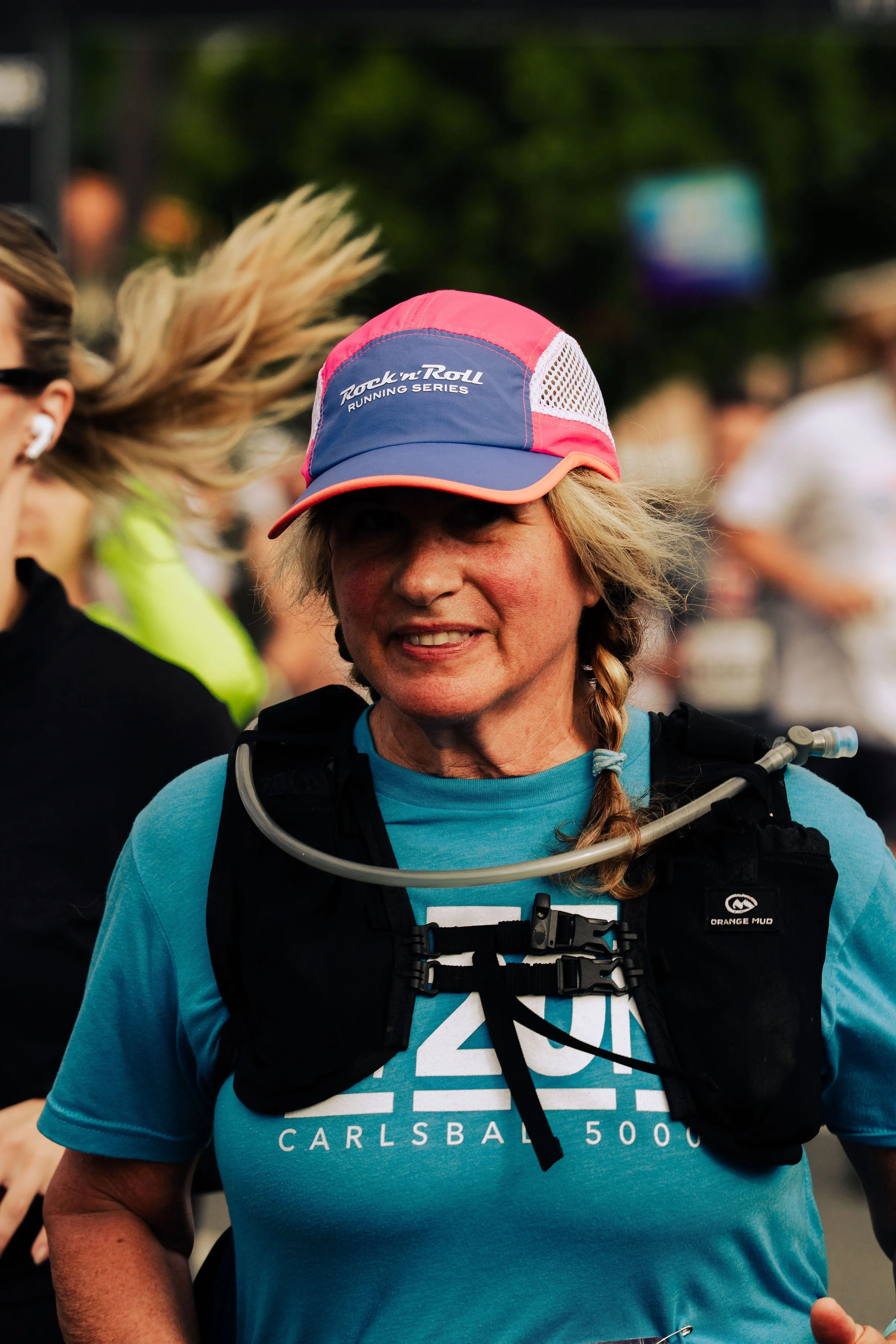 A woman participating in a running event wearing a pink and blue cap with 