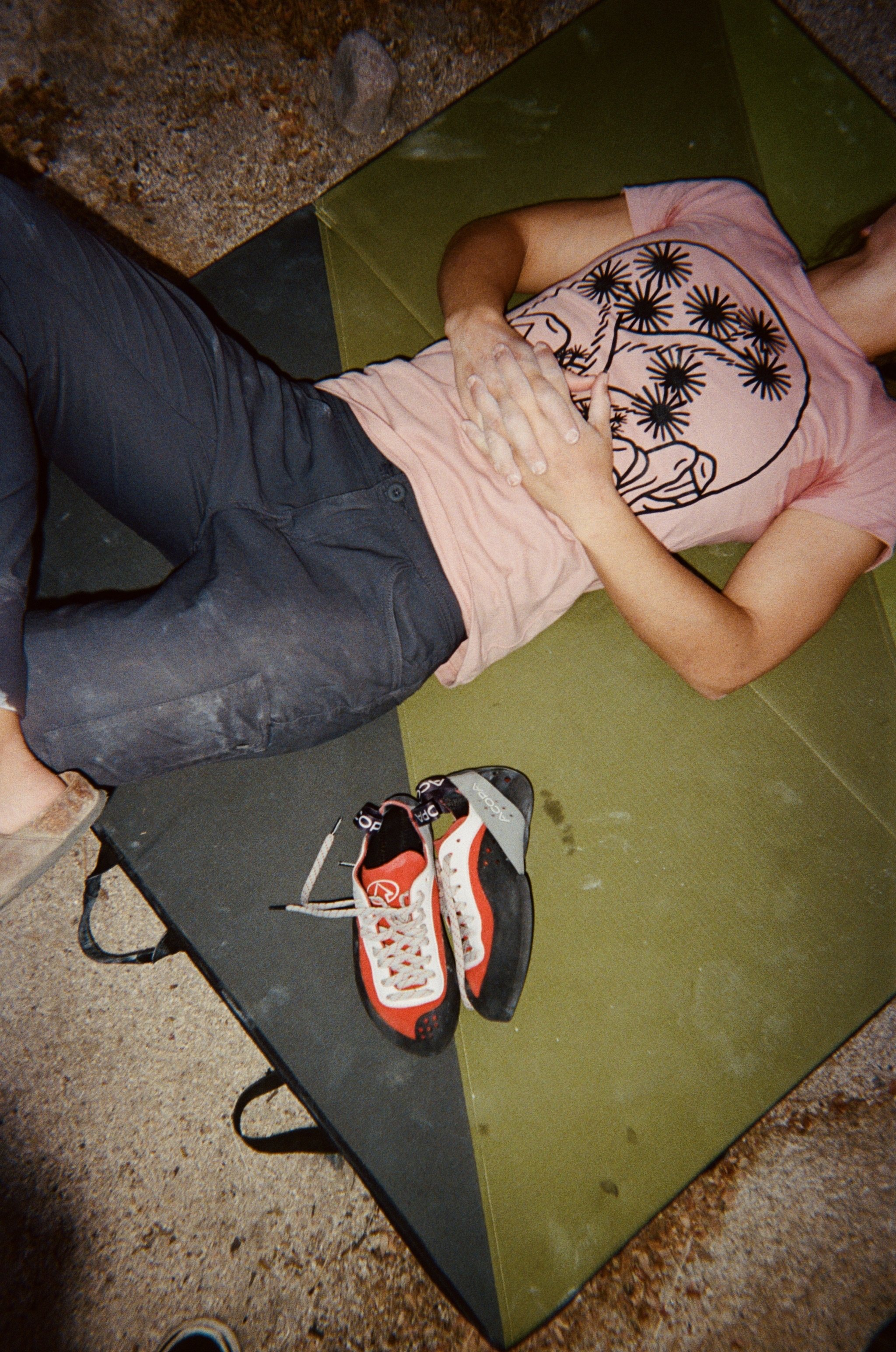 Close-up of a pair of Nike Air Jordan sneakers on a shoe rack, with a person lying on a green yoga mat nearby, hand resting on their stomach, wearing a pink t-shirt with a graphic design, and sneakers and sandals on the ground.