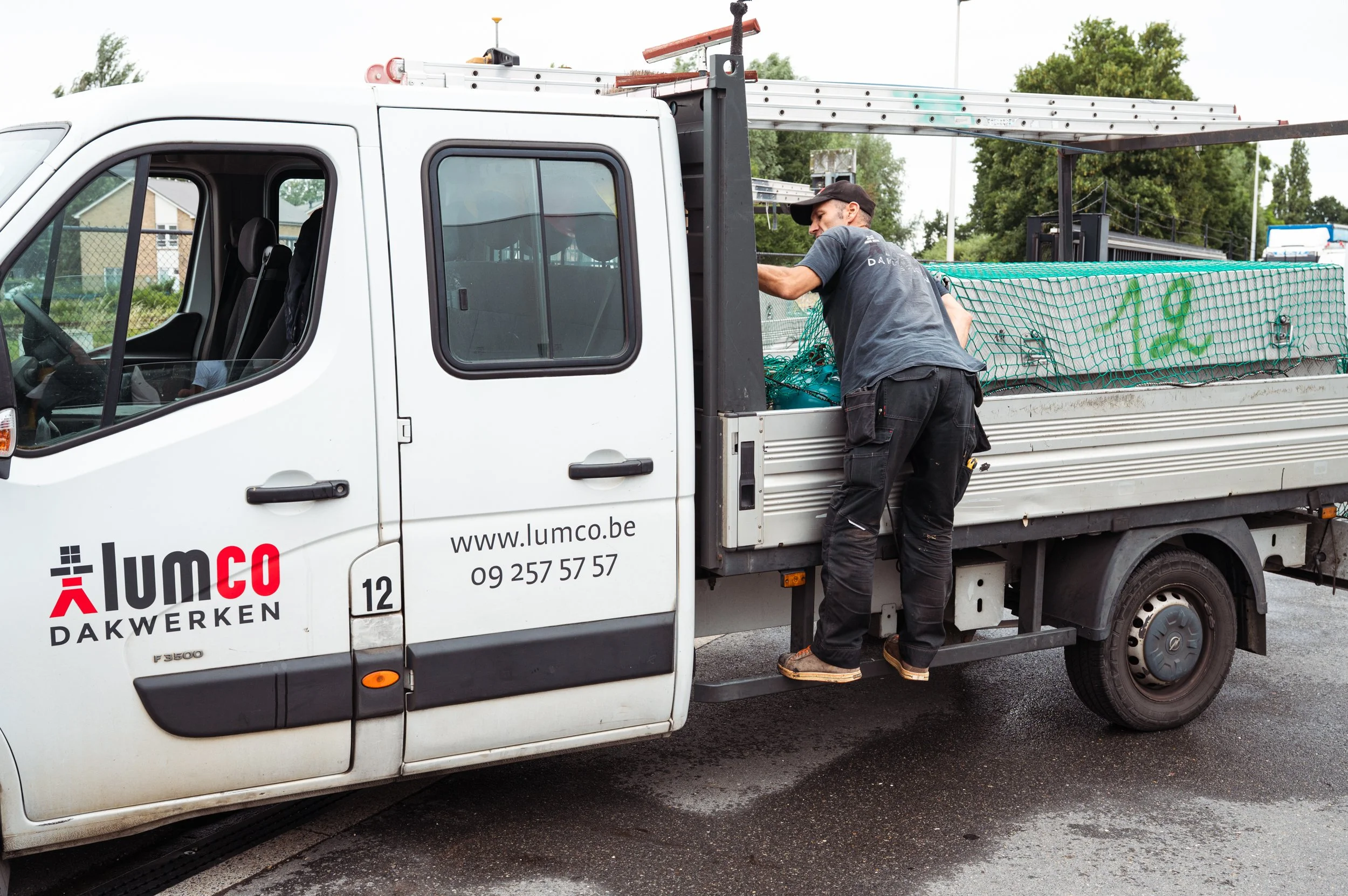 Man laadt materiaal op een werktruck met logo 'lumco dakwerken' voor een doe-het-zelf of bouwbedrijf.