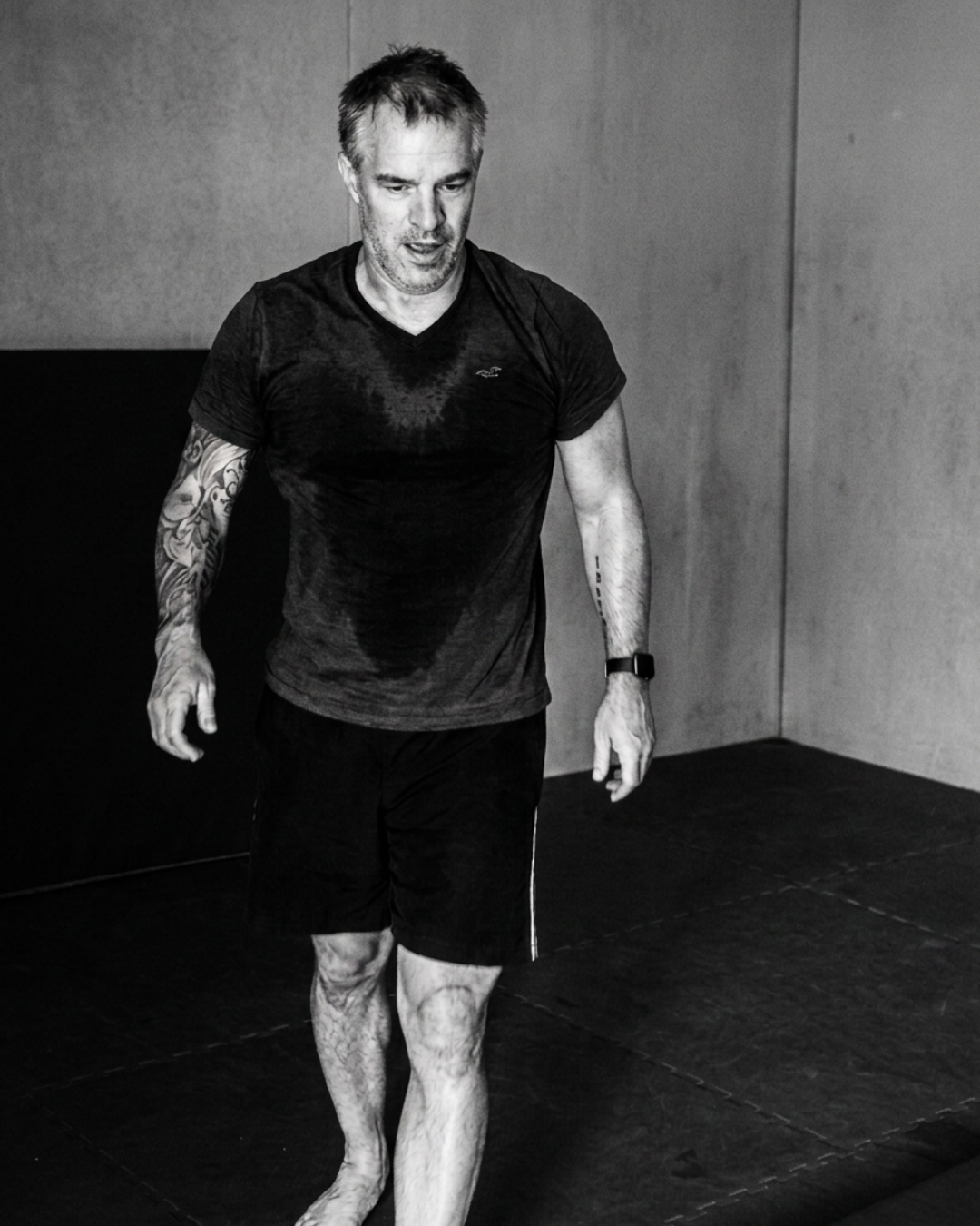 A man in workout clothes walking barefoot on a gym mat.