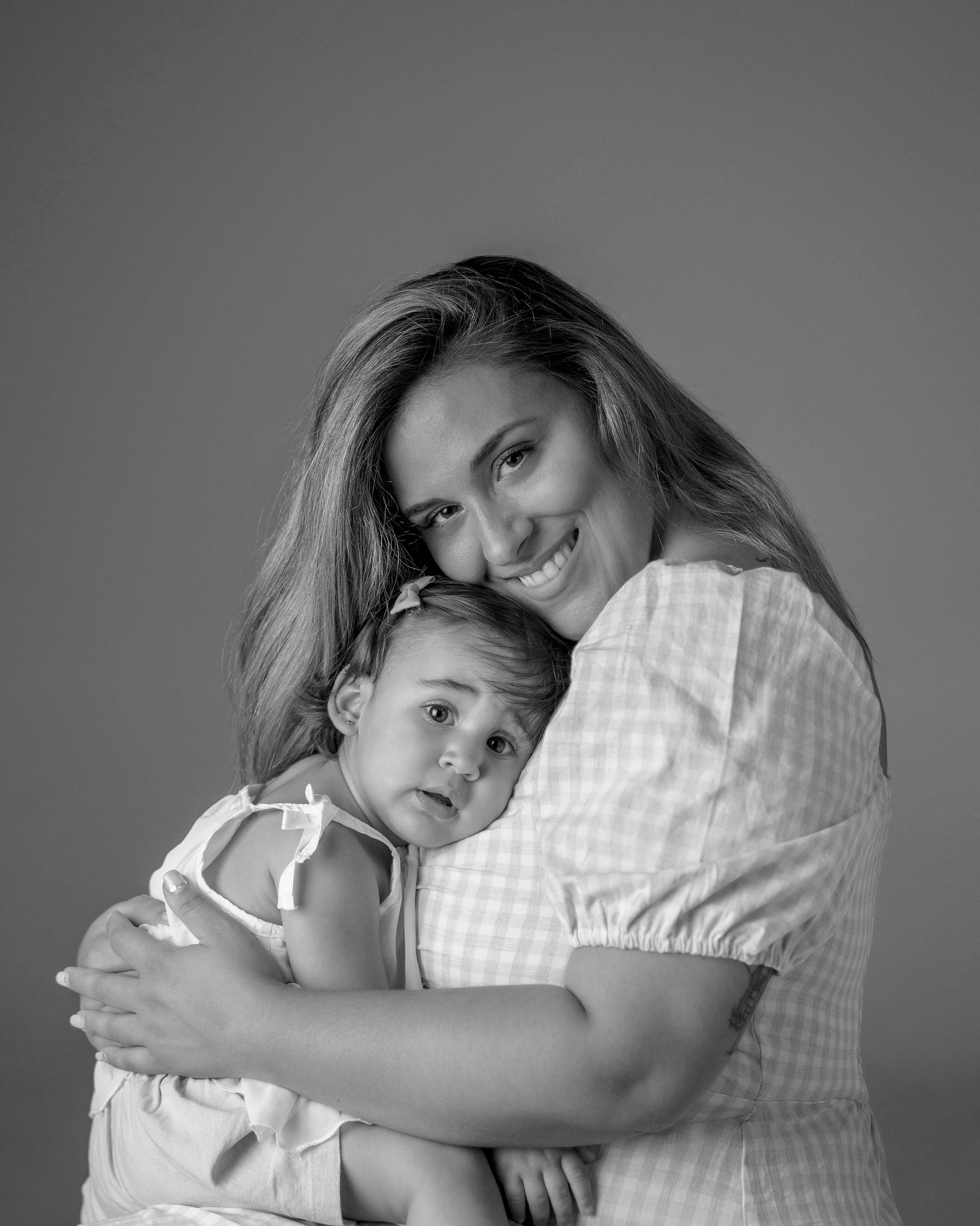 Mujer y niña abrazándose, sonriendo y mirando a la cámara en una fotografía en blanco y negro.