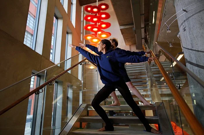 Two women practicing yoga or stretching on a staircase indoors with modern lighting and architecture.