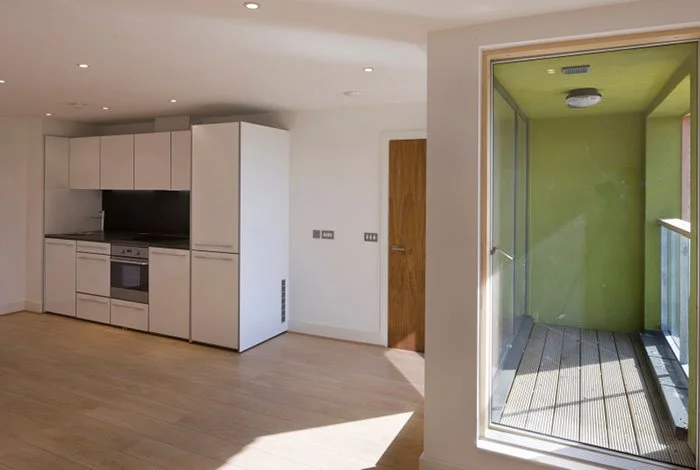 Modern kitchen with white cabinetry and built-in oven, adjacent to a small balcony with green walls and wooden flooring.