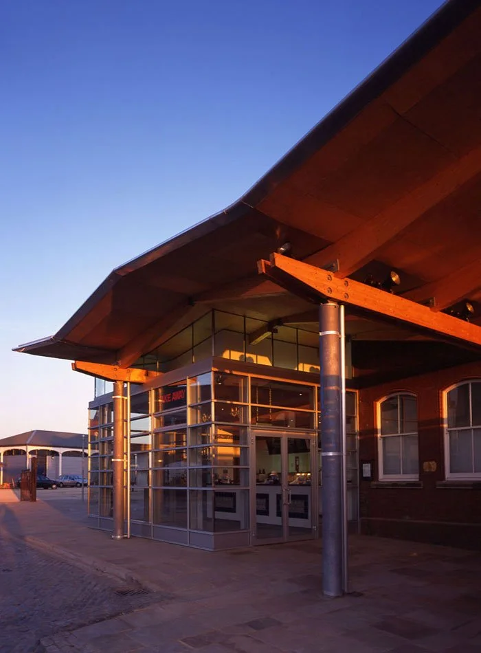 A closeup of the Visitor Centre entrance with glass walls, metal supports and frames, and a large roof overhang at sunset.