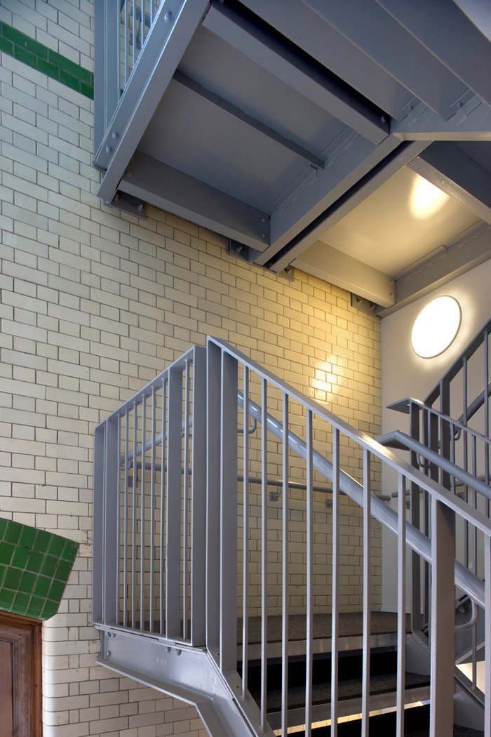 The Pump House interior staircase with metal railings attached to a beige brick work walls and flashes of the dark Green tile highlights.