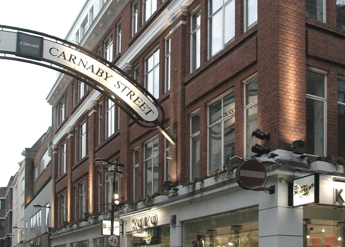 View of a city street corner with a brick building, street sign reading 'Carnaby Street', and storefront signage for 'KOKO' and 'Dr. Martens' at ground level looking out towards Silver House.