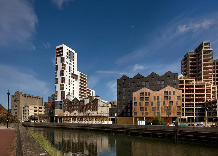 Cityscape with modern high-rise and mid-rise buildings along the river in Ipswich, with the white building of Cranfields Mill standing out on the left, under a blue sky.