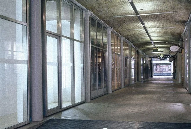 Empty shopping mall corridor at Thomas Neal’s Centre with glass storefronts and bright lighting.