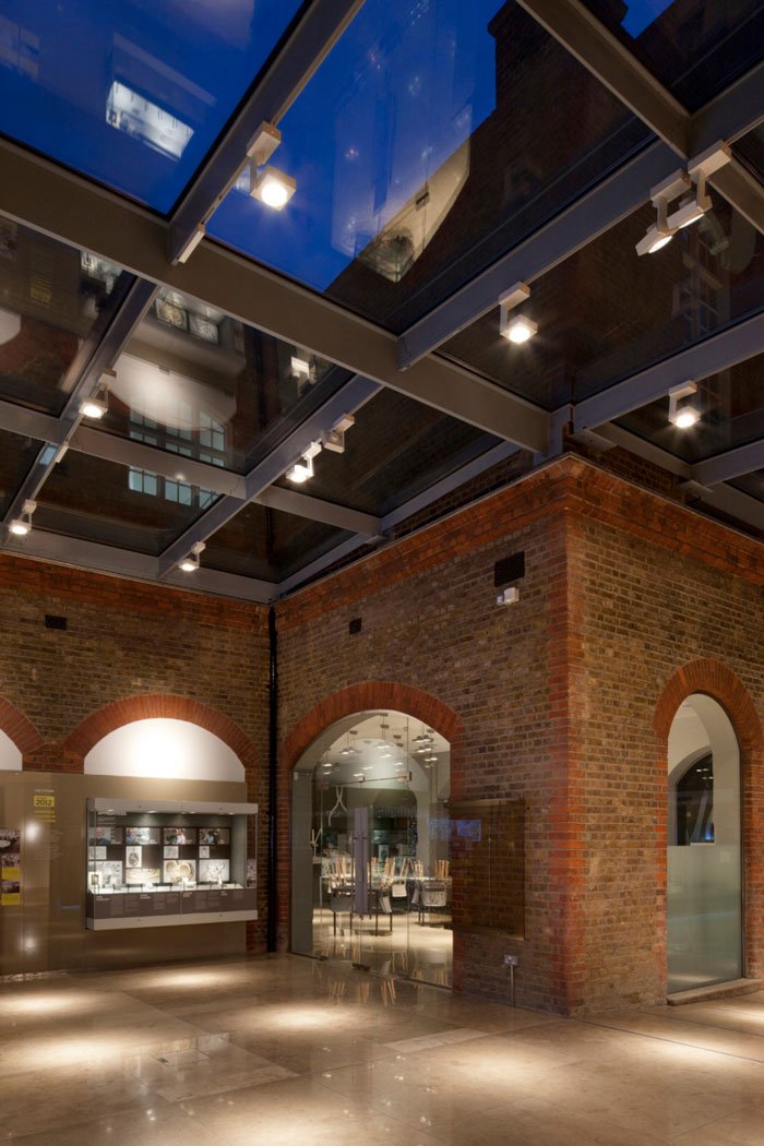 Interior of a modern building with exposed brick walls, glass ceiling panels, and display cases.