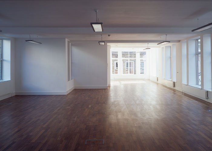 Empty room inside Silver House with large windows, wooden flooring, and ceiling lights.