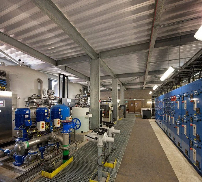Internal workings of the Water Treatment Facility featuring Industrial machinery and control panels inside a building with a metal roof and support beams.