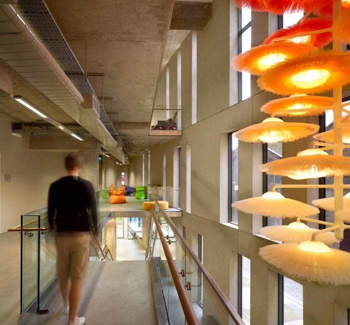 Interior of a modern building with large windows, colorful seating area, and artistic orange and yellow lighting fixture.