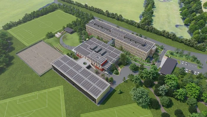 Aerial view of a school complex with multiple buildings, sports fields including soccer and basketball courts, surrounded by greenery and trees.
