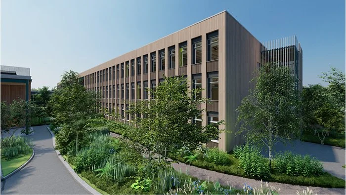 Modern multi-story building with a wood exterior, surrounded by trees and greenery, with a curved pathway in the foreground under a clear blue sky.