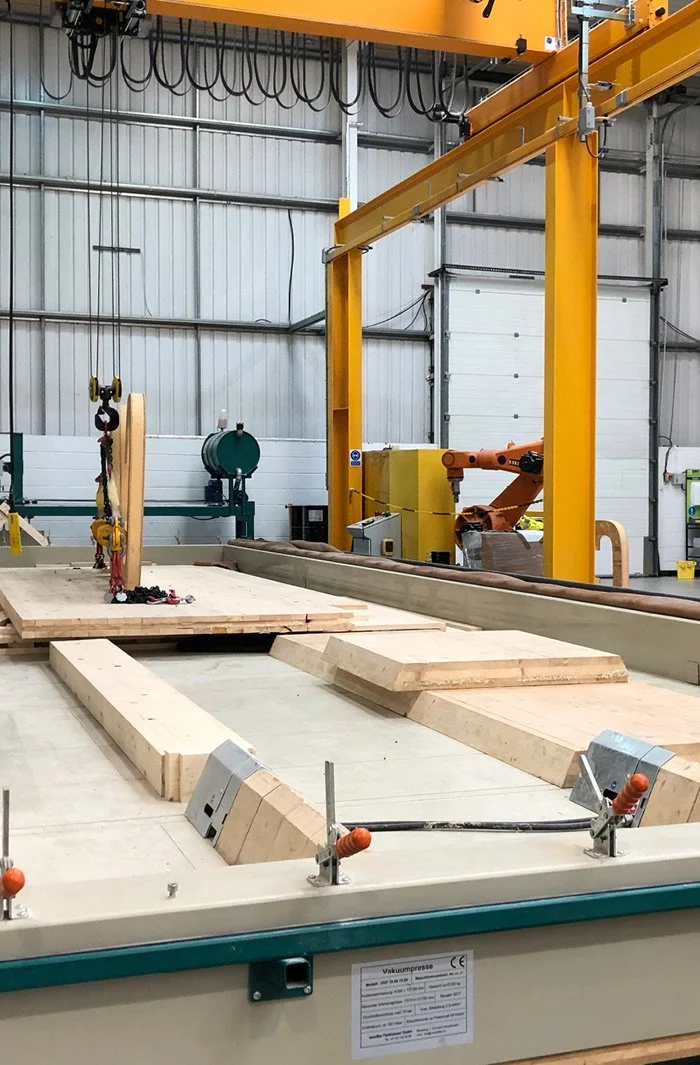 Woodwork factory with large wooden boards, a crane for lifting, and an industrial robotic arm in the background.