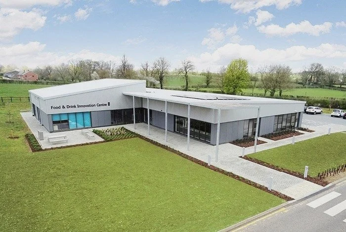 A modern building labeled 'Food & Drink Innovation Centre' with a large lawn and parking lot in the background.
