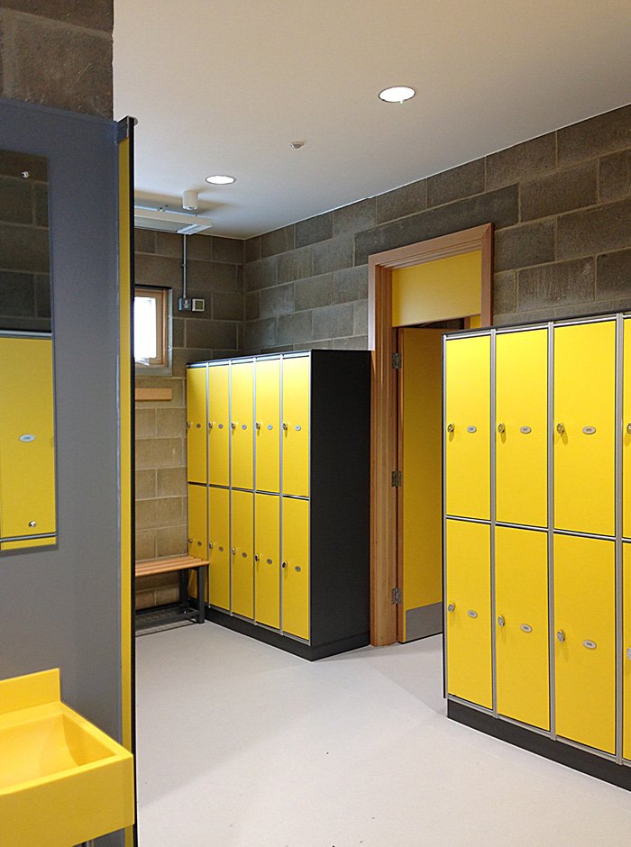 A locker room with bright yellow lockers, a bench, and a small window.