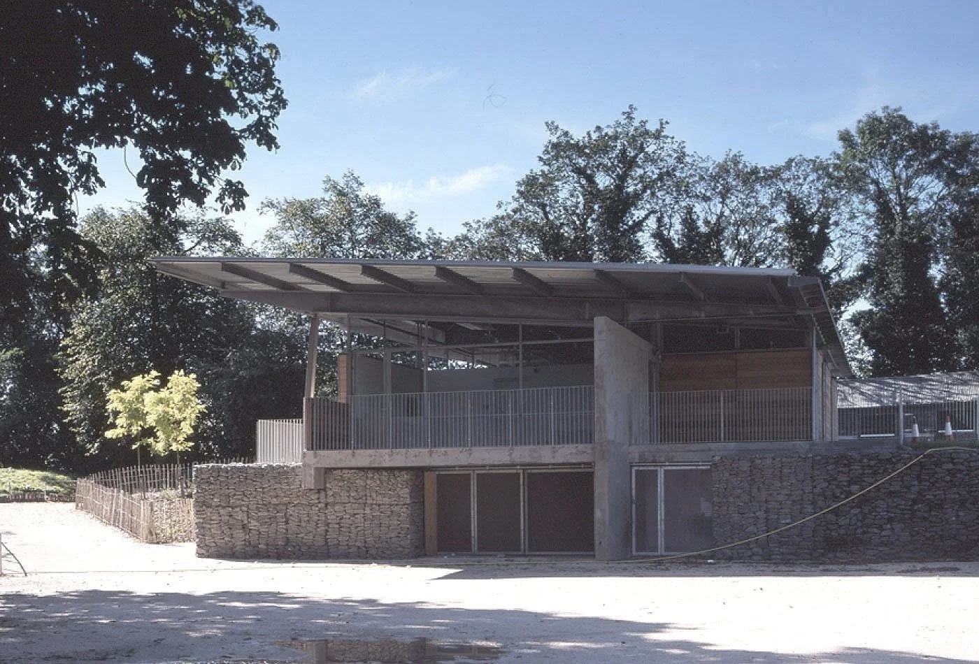 The two-story Crystal Palace Park Renovation with an open upper balcony, stone foundation, and large windows, surrounded by trees.
