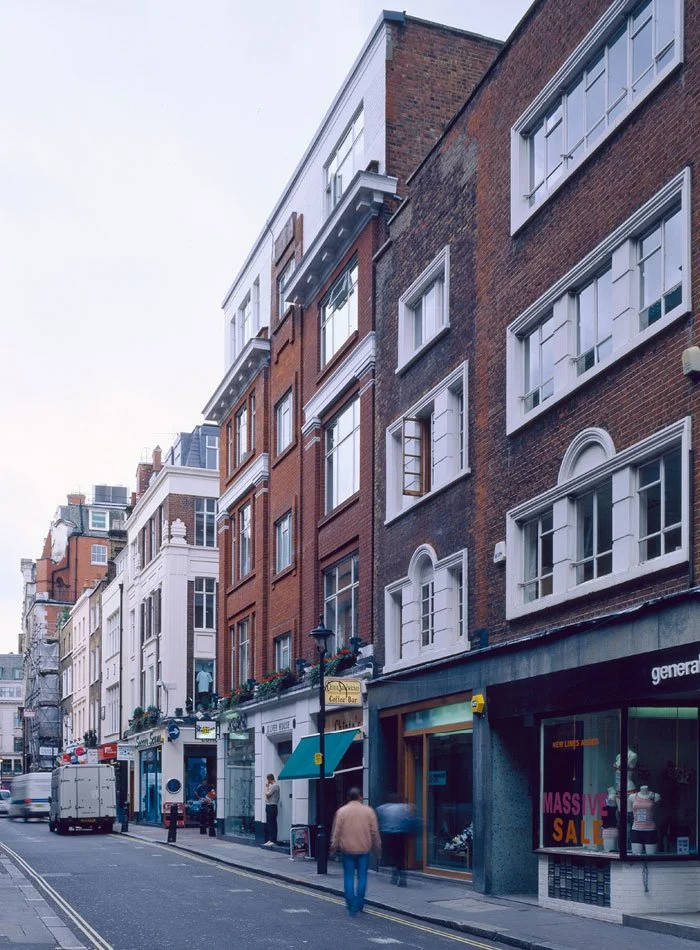 City street scene with multi-story brick buildings, storefronts, and pedestrians walking past Silver House.