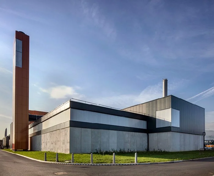 Modern industrial building with a high tower, metal siding, and large windows, set against a partly cloudy sky.