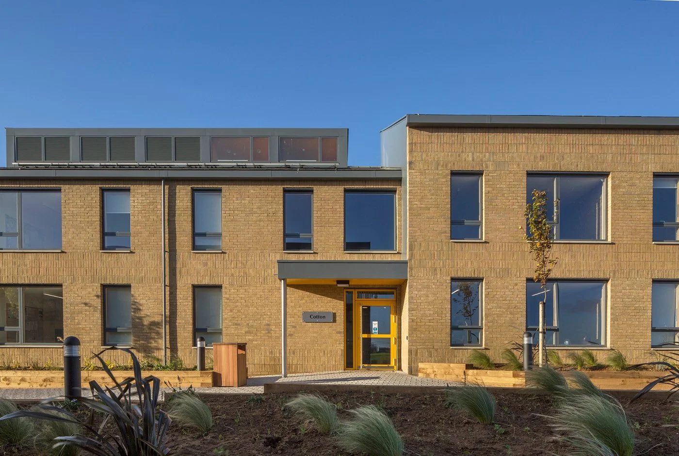 A side view of the entrance to Moulton College Student Housing with large windows and a yellow door, with landscaped garden in front and clear blue sky above.