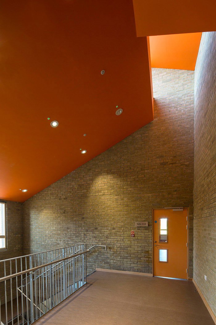 Interior of a building with a staircase, brick walls, and a ceiling with orange paint and recessed lighting.
