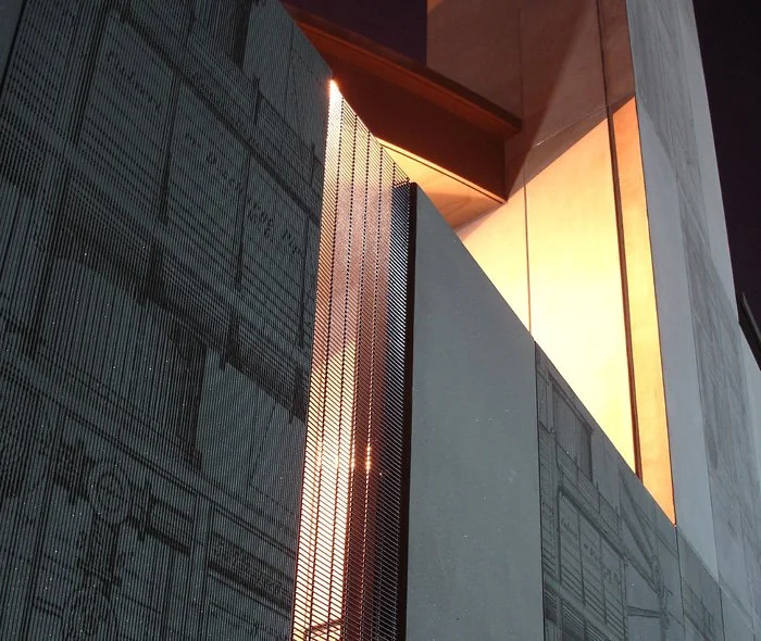 A artistic close-up of a Pudding Mill Pumping Station building facade – featuring some a textured metal see-through panel with warm lighting illuminating the concrete panel elements showing off the external engineering drawings clearly.