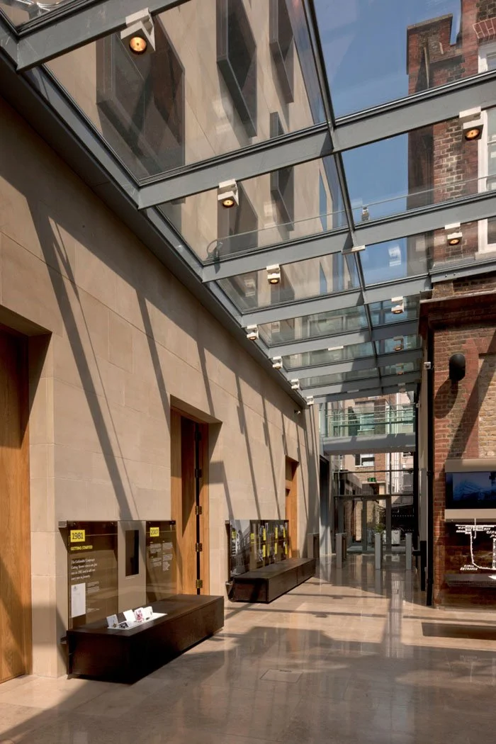 Modern interior with glass ceiling, beige walls, wooden doors, and informational displays along the wall.
