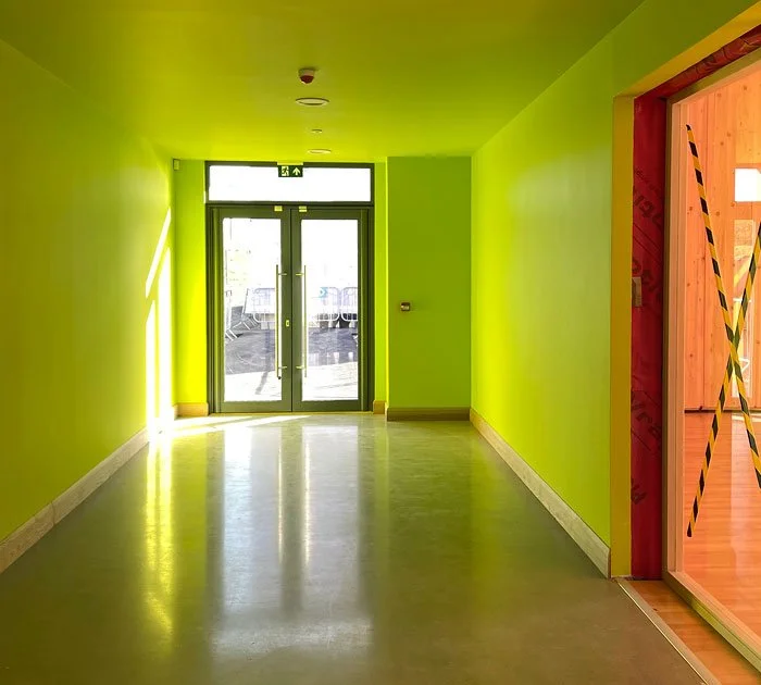 Empty hallway with bright green walls, glass doors at the end, and a wooden frame under construction on the right side.