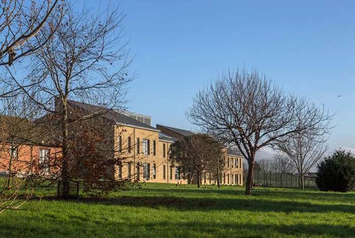 A shot of the Moulton College Student Housing buildings from distance with dark roofs, surrounded by leafless trees and a grassy yard, under a clear blue sky.