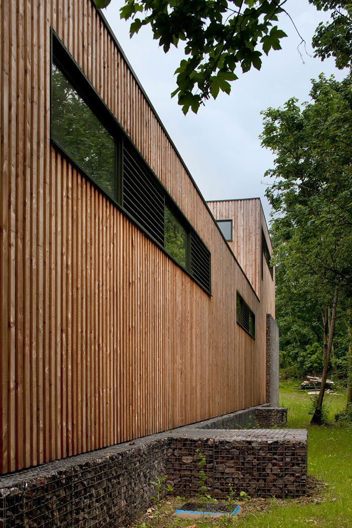 A closeup exterior view of Water Treatment Facility modern building with wooden siding, black window covers, and surrounded by green trees.