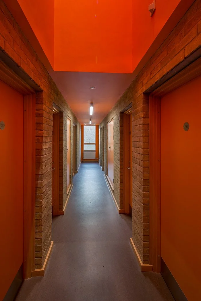 An internal corridor at Moulton College Student Housing with orange doors and brick walls, leading to a window at the end.