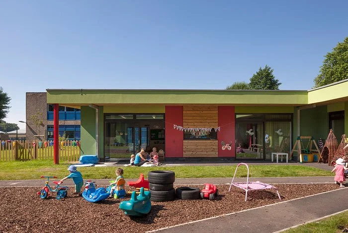 Children playing outside a colourful Enchanted Wood Nursery with toys and outdoor furniture.