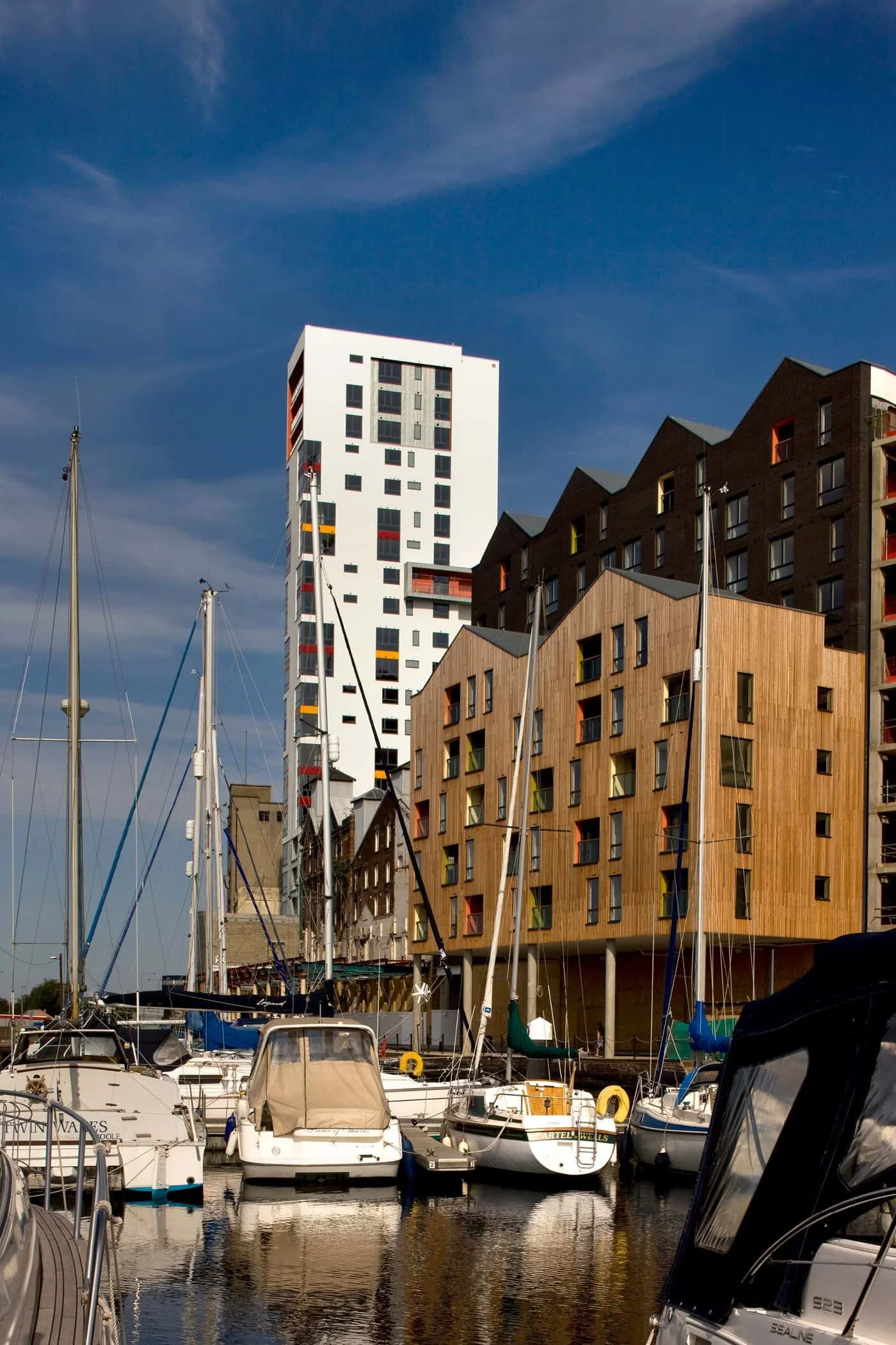 The Albion Wharf Marina with boats docked in the foreground, in the background is the Cranfields Mill Tower modern buildings under a blue sky.