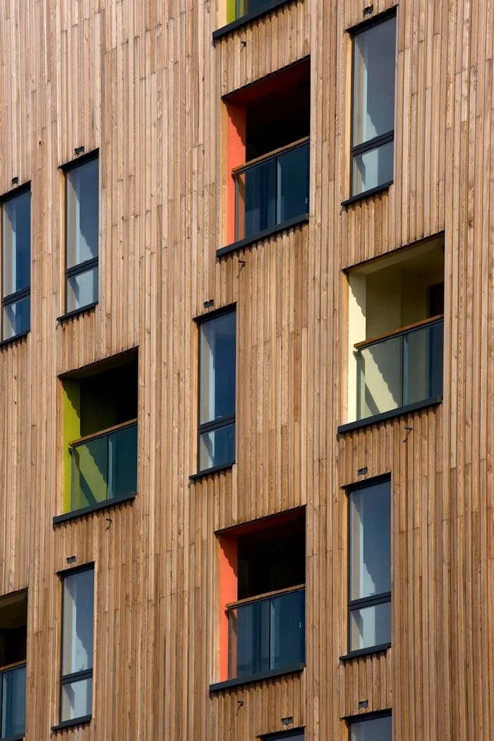 Close-up of a modern multi-story building's exterior with wooden panel siding and multiple windows and balconies with glass railings.