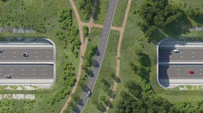 Aerial view of a green park with walking paths, a road, and two covered parking areas.