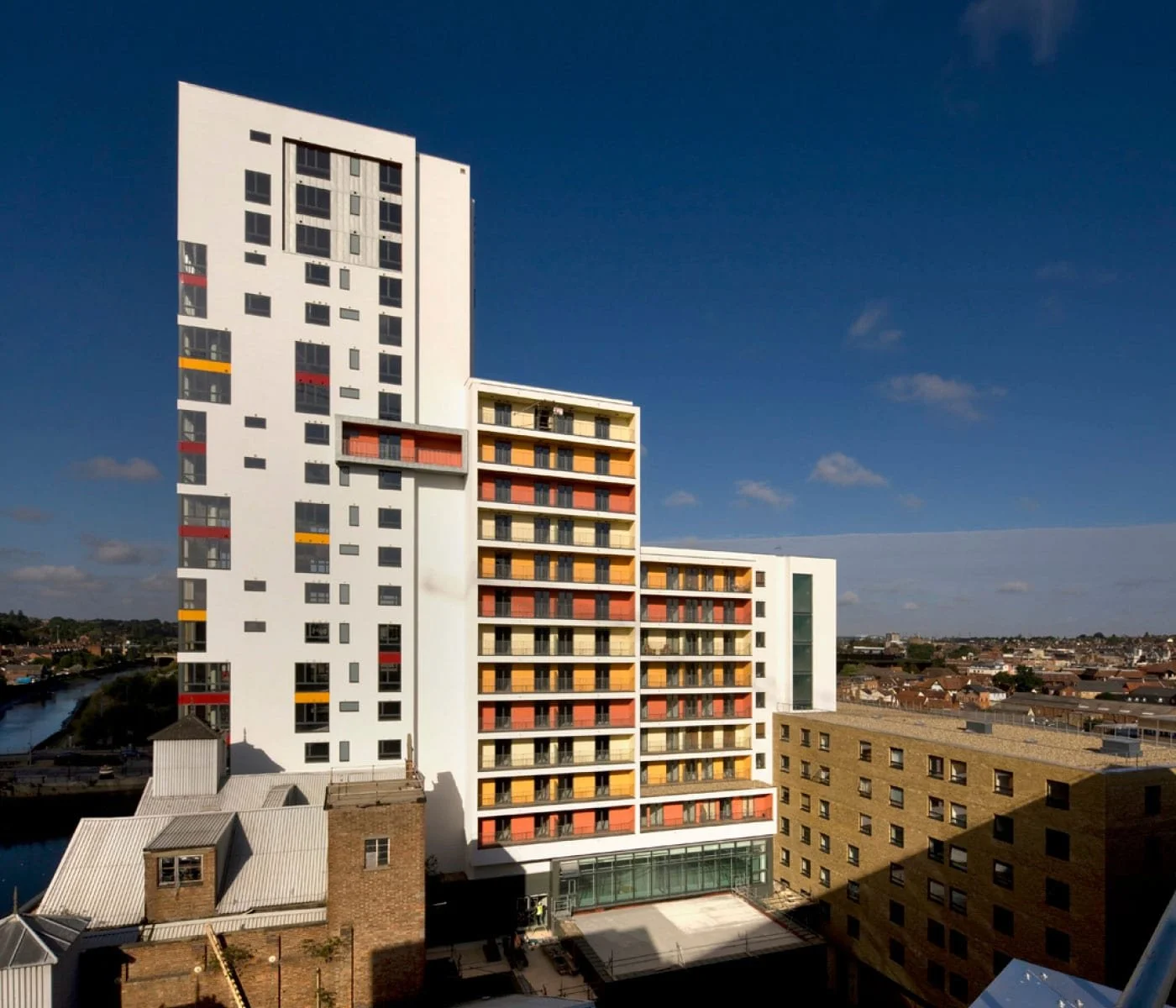 Colorful modern multi-story building with orange, red, yellow, and white accents against a clear blue sky in an urban setting.