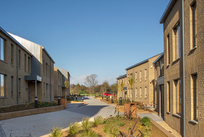 View of a Moulton College Student Housing paved street flanked with brick buildings, landscaped sidewalks, and a clear blue sky.