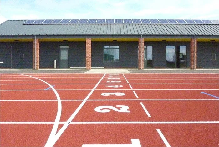Running track with numbered lanes in front of a building with solar panels on the roof.