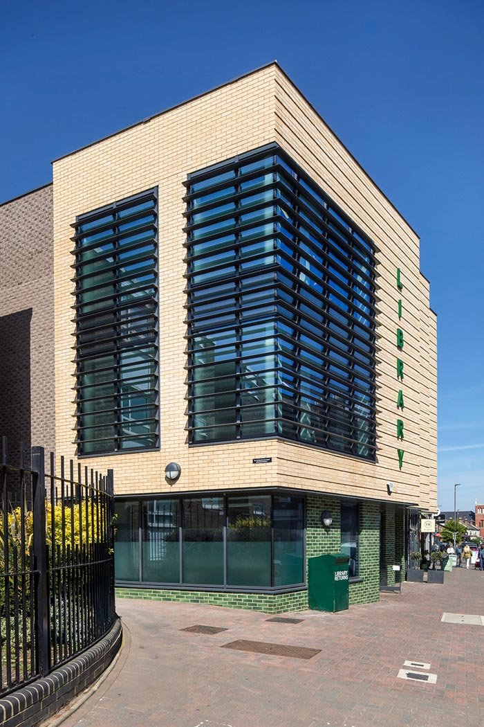 The modern Northcote Library building with beige brick exterior and large glass windows, with green vertical signage that reads 'LIBRARY' and a green library return drop box outside.