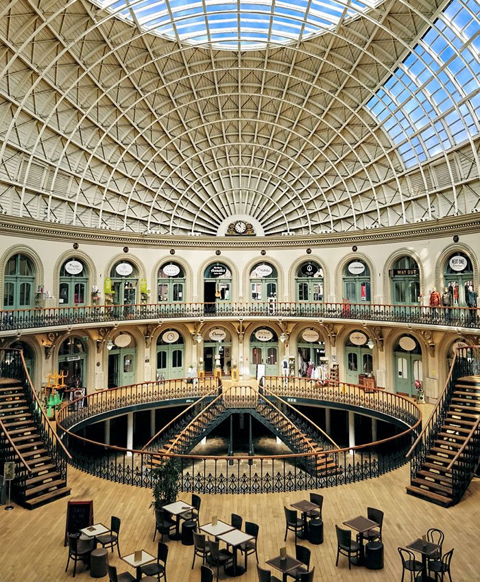 A full landscape interior view of the Grade 1 listed Corn Exchange in Leeds historic shopping arcade with a glass-domed ceiling, multiple levels of shops, and staircases leading to the upper floors.